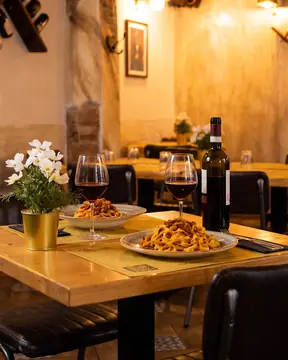 Un tavolo per due in sala, con due piatti di tagliatelle al ragù e due calici di rosso